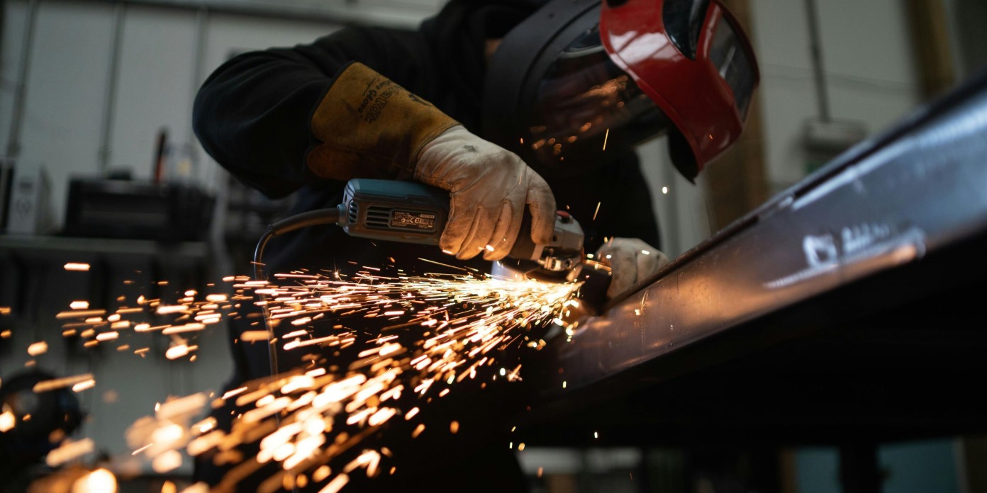Persona usando una amoladora eléctrica sobre una pieza metálica, generando chispas en un taller industrial. Lleva guantes protectores y careta de seguridad.